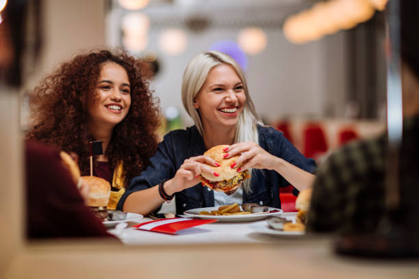 Super ready to dig in Two happy female friends eating burgers in a restaurant fast food restaurant stock pictures, royalty-free photos & images