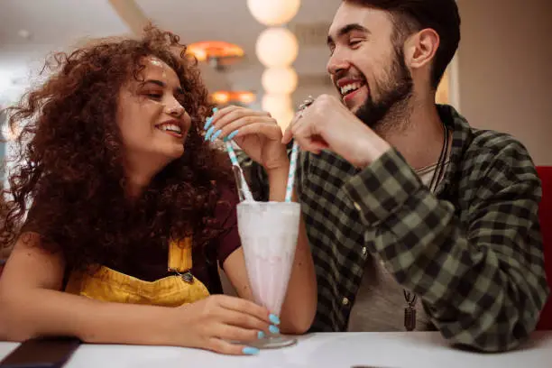 Young happy couple on a date sharing a milkshake in a restaurant