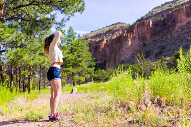 main loop trail with woman standing looking up hiking in bandelier national monument in new mexico in los alamos with canyon cliffs - jemez mountains imagens e fotografias de stock