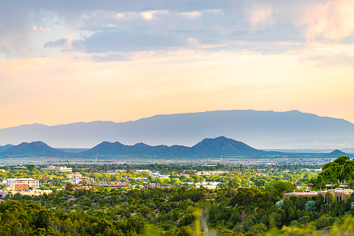 Sunset in Santa Fe, New Mexico skyline with golden hour light on green foliage summer plants and cityscape buildings with mountains silhouette