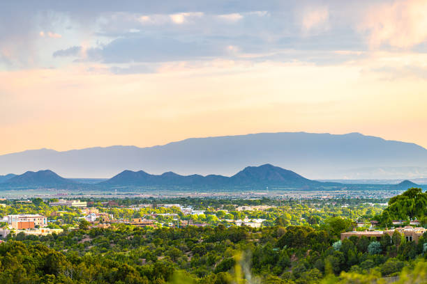 Sunset in Santa Fe, New Mexico skyline with golden hour light on green foliage summer plants and cityscape buildings with mountains silhouette Sunset in Santa Fe, New Mexico skyline with golden hour light on green foliage summer plants and cityscape buildings with mountains silhouette adobe material photos stock pictures, royalty-free photos & images