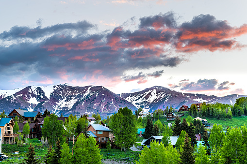 Cityscape of Crested Butte village small mountain town in Colorado in summer with dark morning sunrise clouds and chalet wooden houses on hills with green Aspen trees