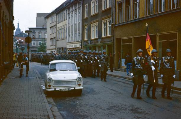 East German military after swearing in of recruits Thuringia (exact location unfortunately not known), German Democratic Republic, 1978. East German military after swearing in of recruits marches through a small town back to the barracks. Also: spectators, buildings and a Trabant (car). east germany stock pictures, royalty-free photos & images