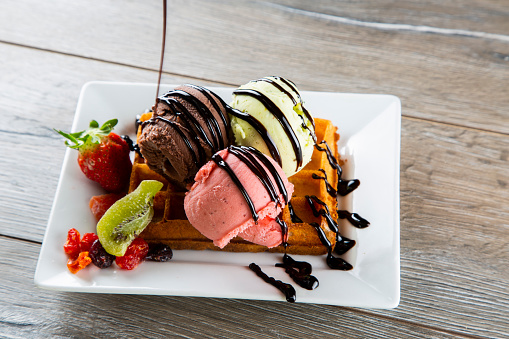 Waffles with fruit ice cream and chocolate sauce on wooden table