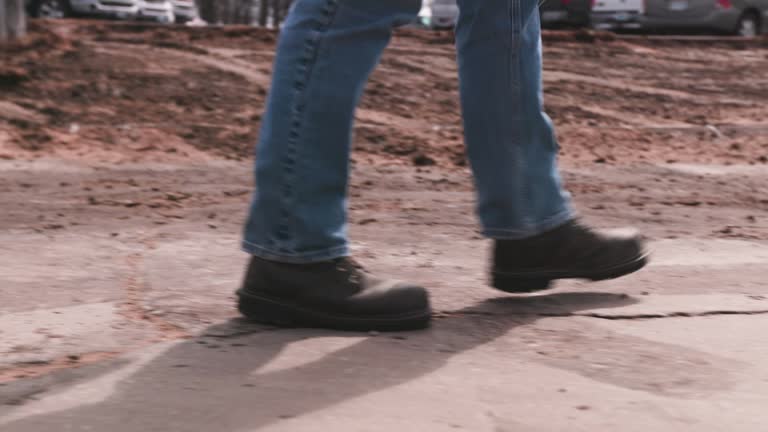 Construction works boots walking down a sidewalk with blue jeans