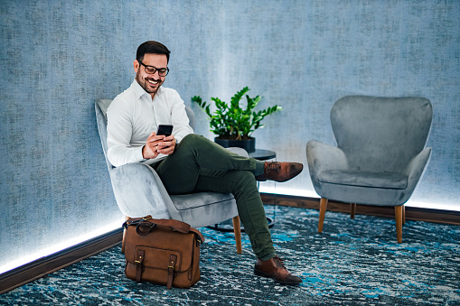 Portrait of a smiling entrepreneur sitting in armchair and using smart phone. Business, elegance, technology and success concept.