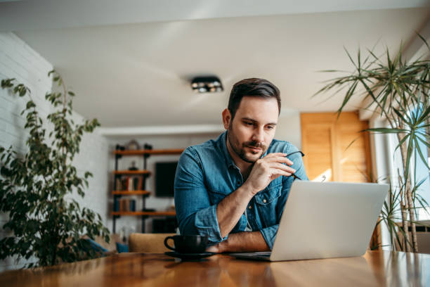 retrato de un empresario ocasional mirando portátil en la oficina en casa. - trabajo freelance fotografías e imágenes de stock