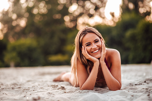 Outdoors portrait of a happy young woman lying on a beach, looking at camera.