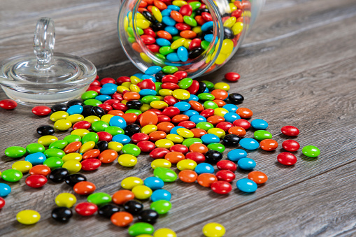 Colorful candies spilled from jar on wooden background