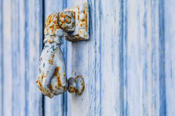 Europe, France, Dordogne, Hautefort. A rusted metal door knocker in the shape of a hand on a blue door in the town of Hautfort.