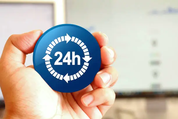 24 hours delivery icon blue round button holding by hand infront of workspace background closeup business concept