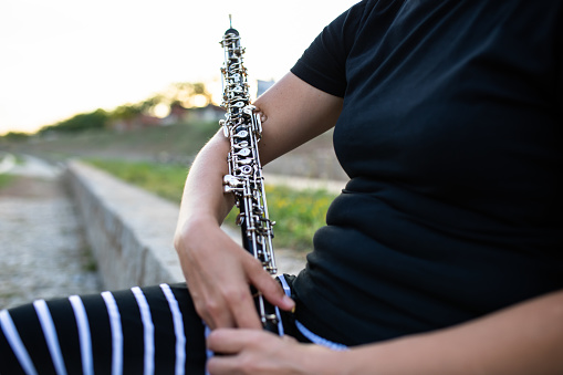 A woman is sitting on a stone wall cradling an oboe