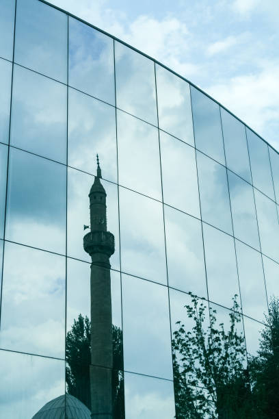 istock Old mosque with its typical minaret mirroring and reflecting on a modern office building in the city center of Prishtina, Kosovo, a city in economic development in the balkans. 1257671534
