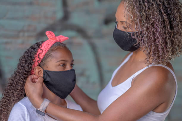 istock African American mother helping daughter put on a protective face mask 1257672896