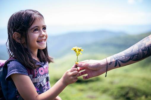 Little beautiful girl is hiking at the mountain smiling and taking a flower  at the background of the nature