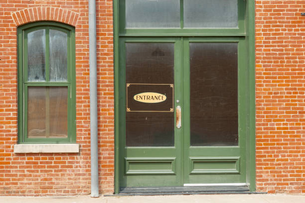 Exterior Art Deco glass and metal doors in white brick wall. Light fixture above doors.