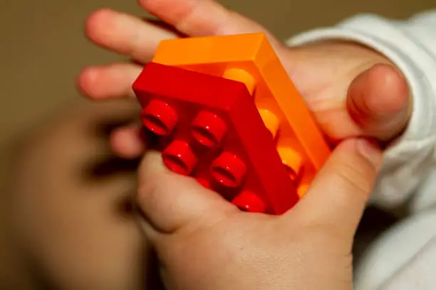 Close up image of an infant baby's hands as he or she is trying to interlock two toy bricks. Image is useful to demonstrate motor development, fine motor skills, balance, precision, baby growth themes