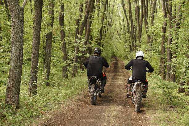 Rear view of unrecognizable people in helmets riding motorbike over rough road in forest