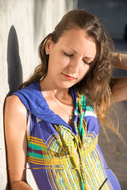istock Young lady looking down with hand on head leaning on wall sunny day 1257699461