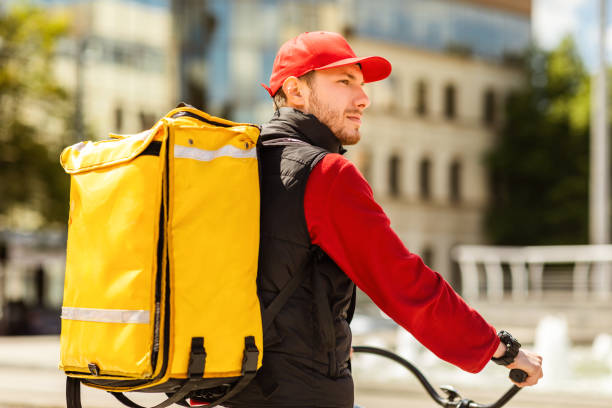 istock Courier With Yellow Backpack Delivering Food On Bicycle Riding Outside 1257703081