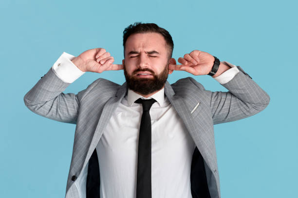 istock Young businessman stressed by noise, closing both ears over blue background 1257703199