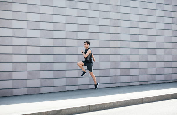 istock Jogging with jumping. Guy runs at path near gray brick wall in city 1257703315
