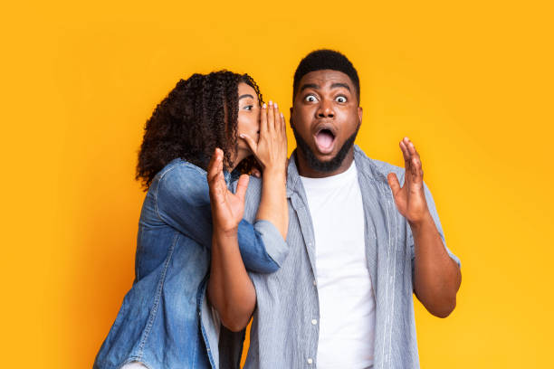 Shocking Offer. Black Girl Sharing Secret With Her Dazed Boyfriend Shocking Offer. Black Girl Sharing Secret With Her Dazed Boyfriend. Surprised Man Opens Mouth In Disbelief Over Yellow Studio Background gossip stock pictures, royalty-free photos & images