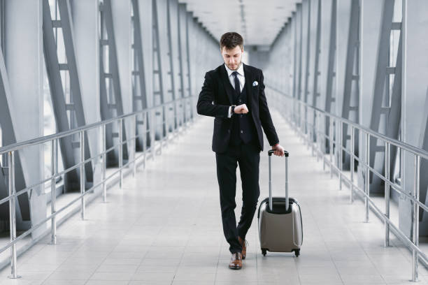 Adult business man standing in airport with suitcase Boarding Time. Confident man checking time on watch, walking with suitcase in airport, going to departure gate smart watch business stock pictures, royalty-free photos & images