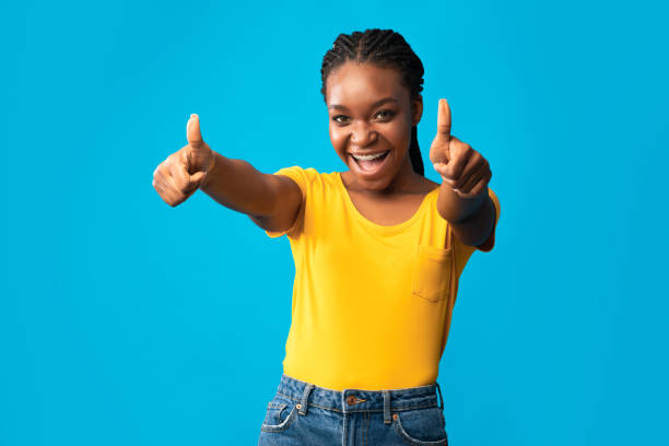 istock Joyful Black Girl Gesturing Thumbs-Up Looking At Camera, Blue Background 1257704553
