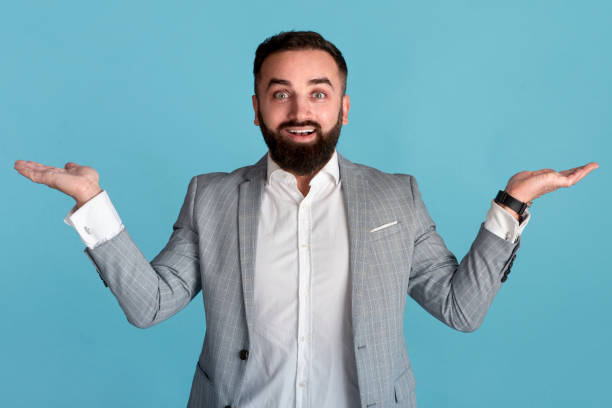 istock Joyful businessman presenting or comparing products, making scales gesture with hands over blue background, copy space 1257705688