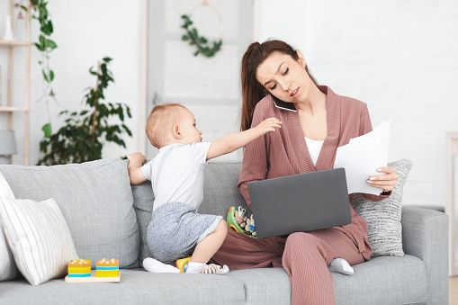 Business And Maternity. Annoyed mom trying to work at home while toddler distracting her, young woman having motherhood stress, free space