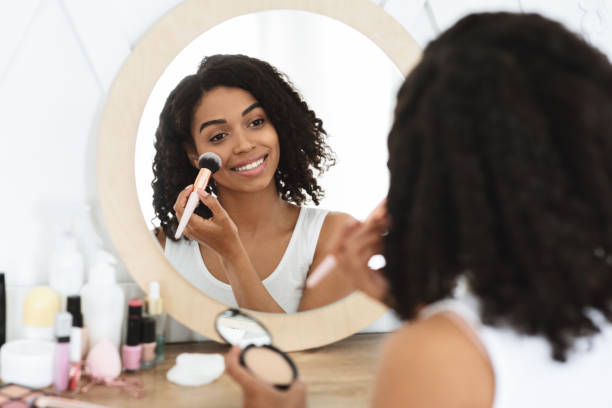 istock Nude Makeup. Smiling Black Girl Applying Blush On Cheeks With Brush 1257709331