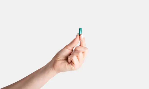 Photo of Unrecognizable young girl showing one blue pill over white background, closeup