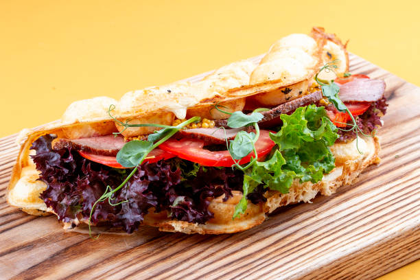 istock Bubble waffle sandwich with ham, tomato and lettuce. On a wooden board. 1257711845