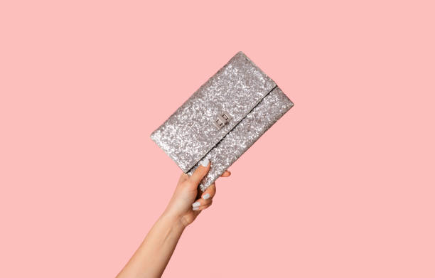 Young woman showing silver sparkly clutch bag on pink background, closeup Young woman showing silver sparkly clutch bag on pink background, closeup of hand clutch bag stock pictures, royalty-free photos & images