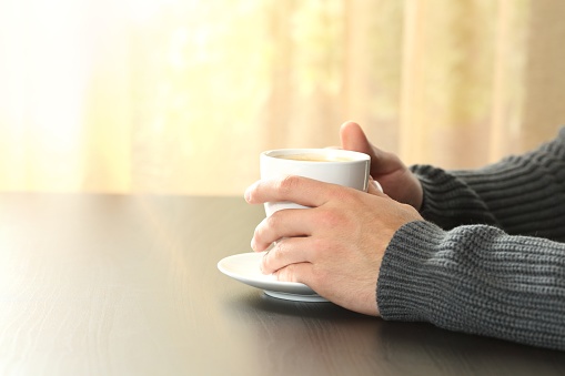 Man hands holding a coffee cup sitting on a table at home