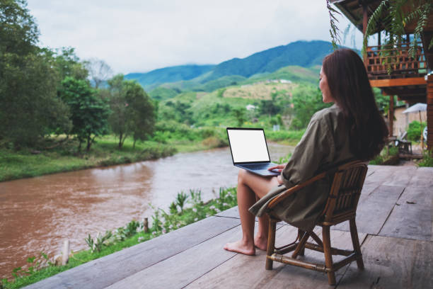istock a young asian woman working on laptop computer while sitting by the river with mountains and nature background 1257714846