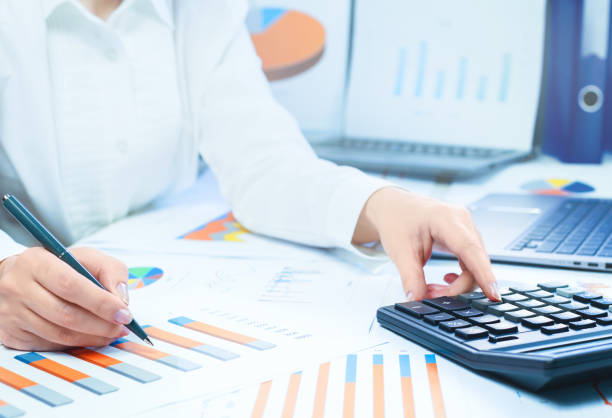 istock Finance. Female hand with calculator on financial graphs on desk 1257717183