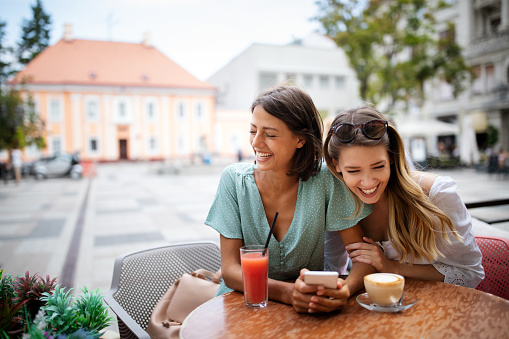 Technology, lifestyle, friendship and people concept. Happy young women with smartphone at outdoor cafe
