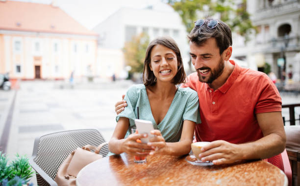 istock Embracing couple using mobile phone, smiling and talking in cafe 1257718069