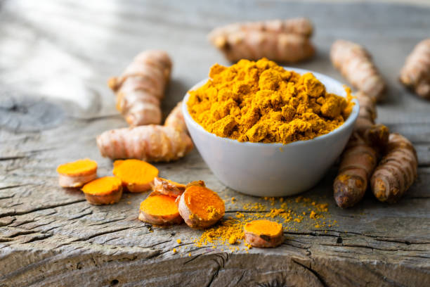 turmeric powder in a white bowl and roots on a wooden table - organic spice imagens e fotografias de stock