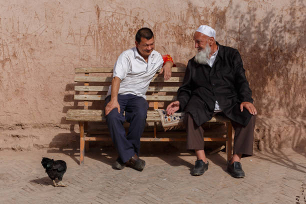 Kashgar, Xinjiang / China - Sept 30, 2017: Two men sitting on a bench having a conversation. Notable detail: the chicken on the left side of the two gentlemen. Part of uyghur minority in China.