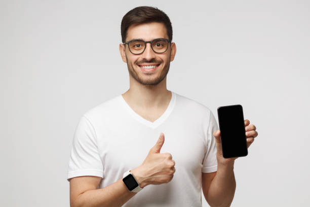 istock Attractive happy young man holding blank smartphone, smiling at camera, showing thumb up gesture, isolated on gray background 1257722792