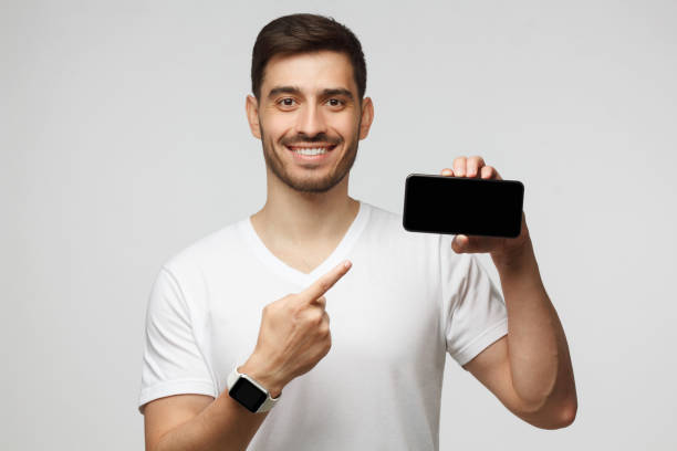 istock Young handsome man showing phone with blank screen with copy space and pointing to it with finger, isolated on gray background 1257722797