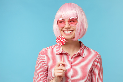 Young girl holding lollipop candy in hand, isolated on blue background
