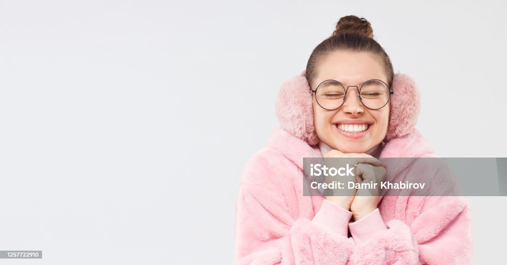 Normal subtraktion oprindelse Horizontal Banner Of Young Smiling Girl Wearing Pink Furry Coat Earmuffs  And Glasses Smiling With Eyes Closed Making Wish Isolated On Gray  Background Copy Space On Left Stock Photo - Download Image
