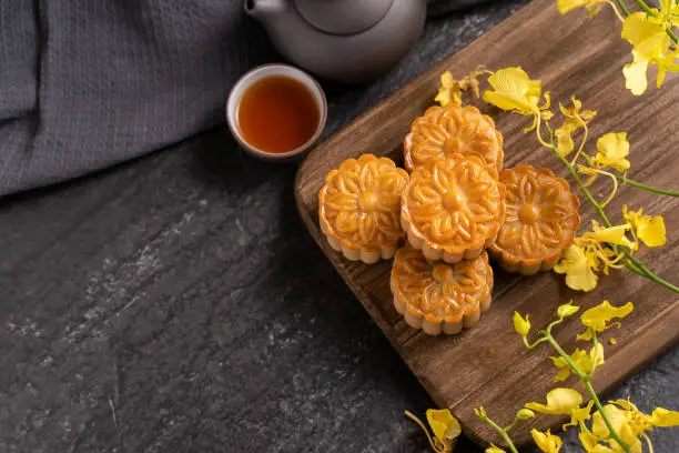 Mooncake, Moon cake for Mid-Autumn Festival, concept of traditional festive food on black slate table with tea and yellow flower, close up, copy space.