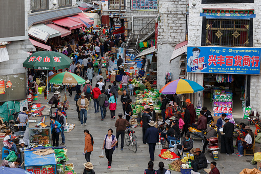 Lhasa, Tibet / China - Jul 29, 2017: View on crowded street market in an alley of Tibet's capital Lhasa. People shopping, stalls with vegetables and fruits for sale. Colorful and bustling scene.