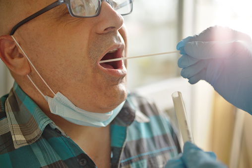 Close up view of doctor hands with medical gloves, holding COVID-19 Throat swab test kit.