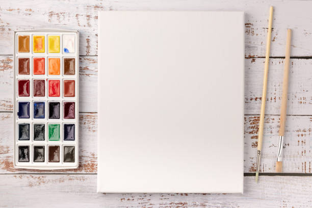 istock Watercolor paints, brushes  and white canvas on wooden background. Copy space. Top view. 1257726556